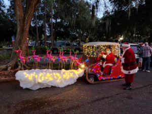 Santa on golf cart sled pulled by 9 flying pink flamingos with antlers, one with a glowing red nose, at the Lakes at Leesburg annual golf cart parade